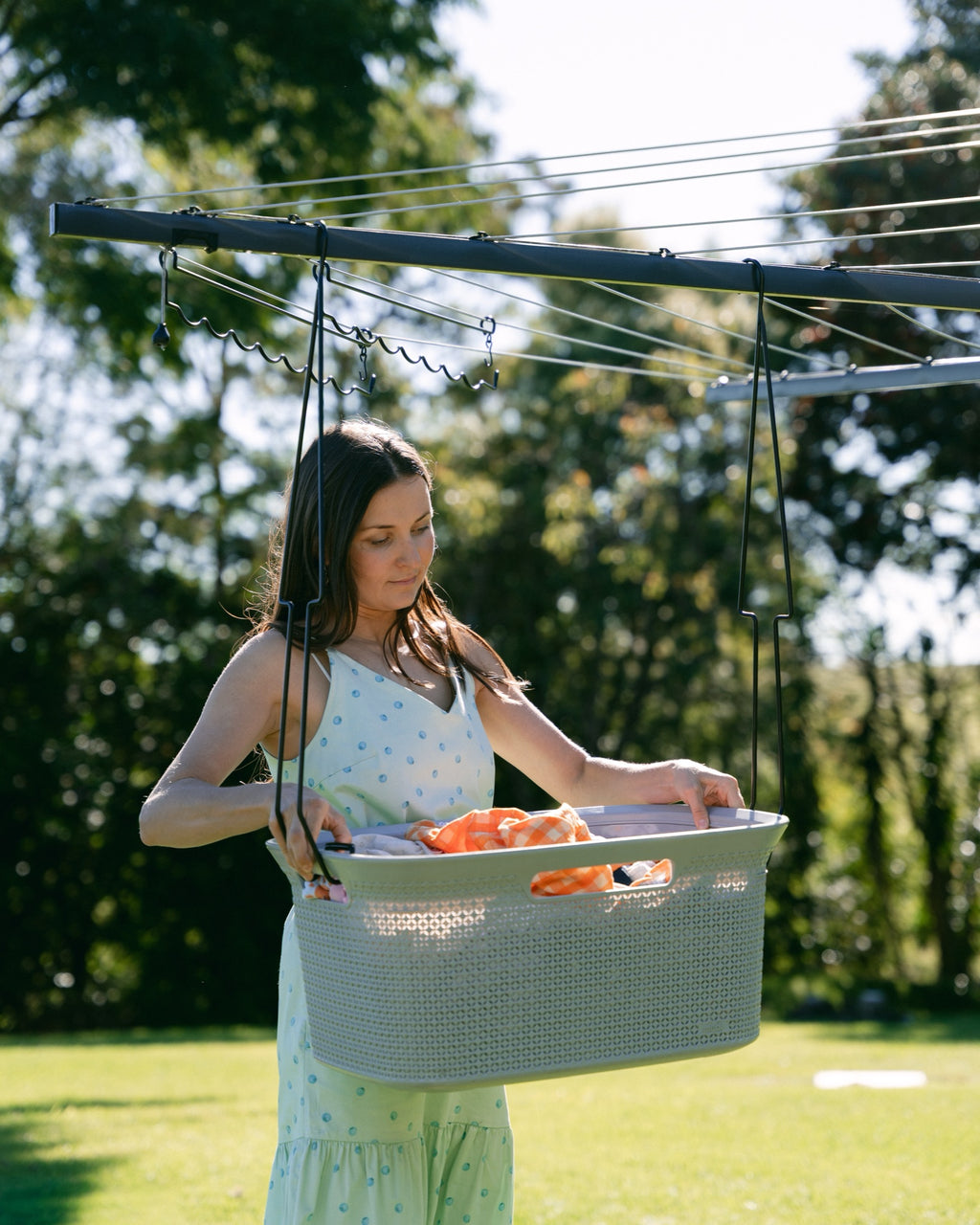 Woman hanging washing in a sunny backyard with her basket at waist height on a rotary clothesline